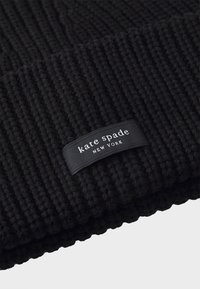 Čierna pletená čiapka s rebrovanou textúrou. Má tkanú nášivku s nápisom "kate spade NEW YORK" bielym textom na čiernom pozadí.