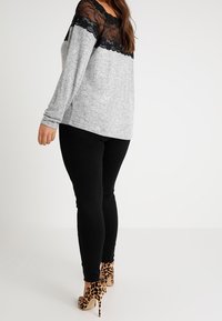 Maglia grigia a maniche lunghe con spalle in pizzo nero, abbinata a leggings neri e scarpe décolleté con stampa leopardata. Tessuto strutturato, vestibilità comoda.