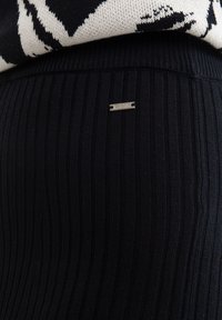 Juodos smulkios raukšlėtos legging'os su glotnia tekstūra ir maža sidabrinė logo etiketė "BIGSTAR" ant juosmens.