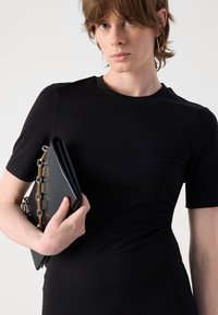 Top aderente nero a maniche corte con scollo rotondo. Abbinato a una pochette nera, con dettagli in catena dorata lungo il lato.