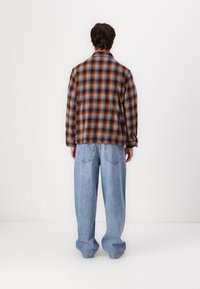 Brown and blue plaid flannel shirt, relaxed fit, paired with light blue baggy jeans. Visible back seams and pockets on jeans.