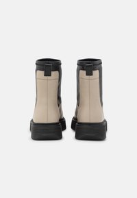 Dos botines que presentan una combinación de colores beige y negro, hechos de cuero suave, con una suela de goma y tiradores en la parte trasera.