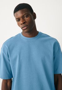 Égkék rövid ujjú póló puha anyagból, kerek nyakkivágással. Laza szabású, minimális varrási részletekkel.