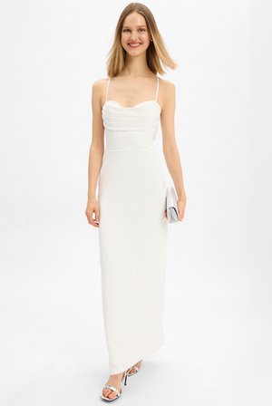 Weißes Maxikleid mit tailliertem Oberteil, plissierten Details an der Brust, dünnen Trägern und einem glatten, fließenden Rock. Kombiniert mit silbernen High Heels.