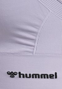 Lichtpaarse sport-BH met ribbelstructuur, voorzien van zwart "hummel"-logo aan de onderkant. Gestructureerd ontwerp met naden voor ondersteuning.