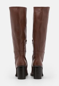 Botas de cuero marrón hasta la rodilla con una textura suave, tacón cuadrado alto y cremalleras laterales para el cierre, exhibiendo un diseño ajustado.