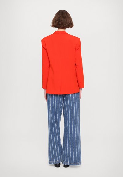 Red blazer with structured shoulders, paired with blue wide-leg striped pants. Smooth fabric, prominent stitching, and a sleek back design.