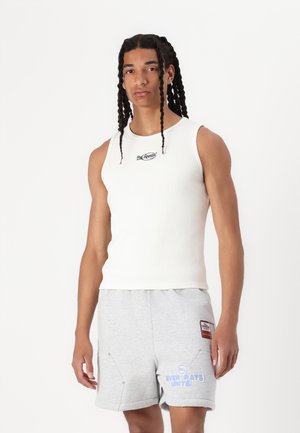 Weißes, geripptes Tanktop mit Rundhalsausschnitt und kleinem Logo auf der Brust, kombiniert mit grauen Shorts mit grafischem Text und Seitentaschen.