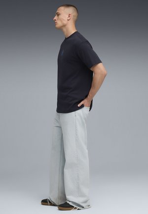 Marineblå crew-neck T-shirt med korte ærmer, parret med lyseblå brede jeans og sorte sneakers; afslappet pasform med minimalistisk design.
