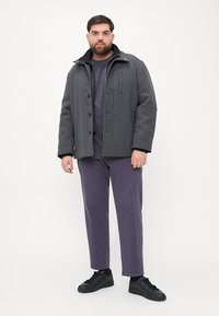 Palton gri din lână, cu un guler înalt, închidere cu nasturi și buzunare laterale, asortat cu un top gri închis și pantaloni mov, purtat cu adidași negri.