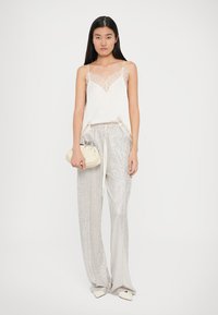 Camisolă din satin alb cu detalii din dantelă, asortată cu pantaloni largi din satin cu mărgele argintii și o poșetă crem. Modelul stă pe un fundal simplu.