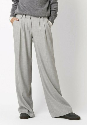 Graue, hellgraue Nadelstreifen-Hosen mit weitem Bein, vorderen Falten und seitlichen Taschen, kombiniert mit einem grauen Pullover und dunklen Sneakers.