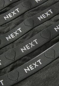Bandes en tissu noir avec "NEXT" imprimé en blanc, présentant un accent de cœur texturé. Texture lisse avec une finition mate.