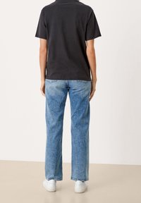 Svart t-shirt med kort ärm i kombination med ljusblå raka jeans och vita sneakers, som visar en avslappnad passform och klassisk design.