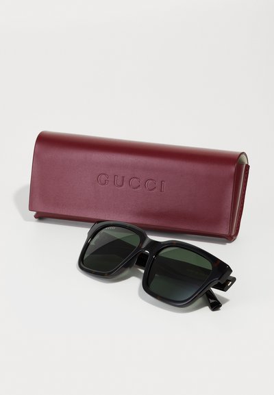Gucci prillid musta kilpkonna vormiga raamis ja roheliste läätsedega, kaasas marooni värvi nahkkate, millel on sisse vajutatud "GUCCI."