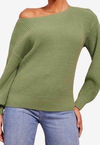 Pull tricoté vert à épaules dénudées avec une texture côtelée et des manches longues, assorti à un jean bleu clair. Le tissu semble doux et épais.