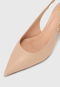 Bežové kožené slingback lodičky s špicatou špičkou a vykrojenými stranami. Hladký povrch s minimálnym šitím a nízkym podpätkom.
