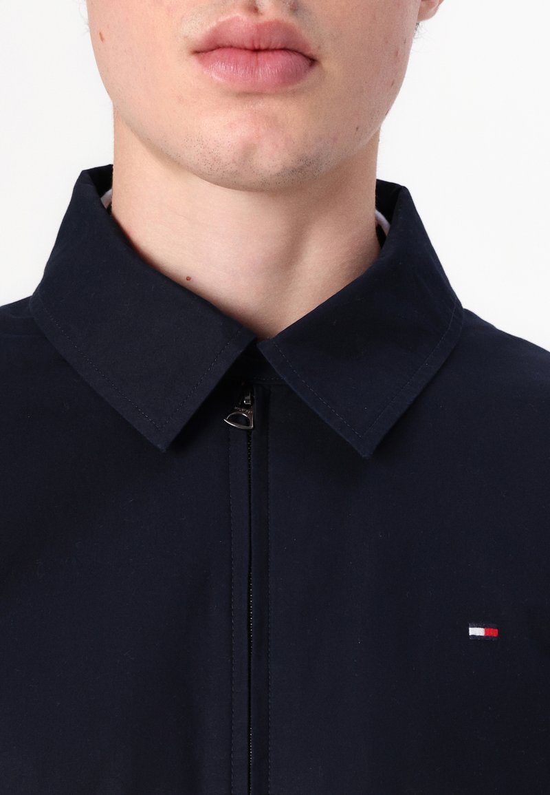 Marinejacke mit hohem Kragen, Frontreißverschluss und kleinen Logodetails in Rot, Weiß und Blau auf der linken Seite. Glatte Textur.