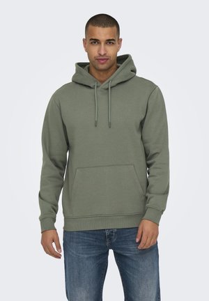 Olive green hoodie made of soft fabric, featuring a front pocket, drawstring hood, and ribbed cuffs. Paired with blue denim jeans.