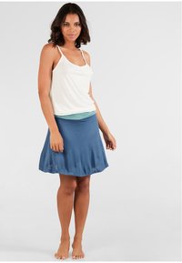 Top bianco senza maniche con spalline sottili abbinato a una gonna blu caratterizzata da un design morbido e fluido. L'outfit presenta uno strato sottostante verde a strati.