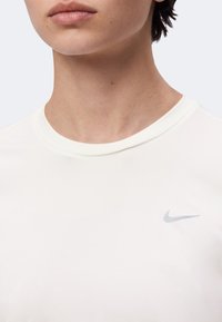 Κοντινό πλάνο ενός ατόμου που φοράει λευκό T-shirt Nike, δείχνοντας το λαιμό, το κάτω μέρος του προσώπου και το λογότυπο της Nike στο στήθος.