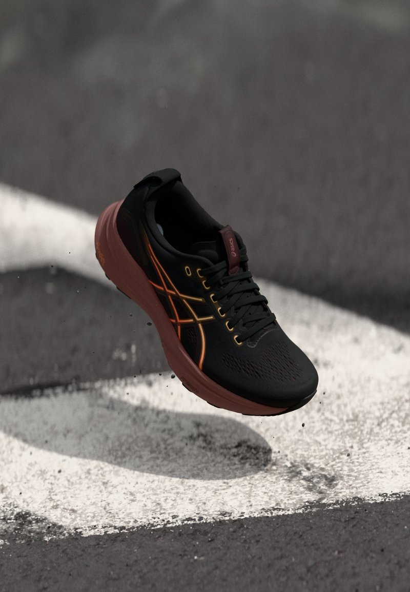 Chaussure de course noire et orange flottant au-dessus d'une surface d'asphalte noire avec un marquage circulaire peint en blanc.