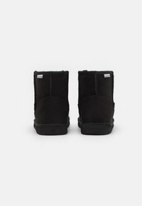 Schwarze Knöchelstiefel aus Wildleder mit einer weichen Textur. Sie haben eine abgerundete Zehe, gestickte Details und eine Gummisohle. Etiketten an den Seiten.