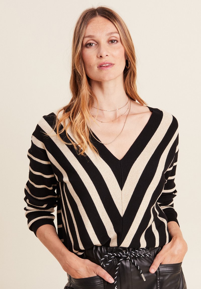 Pull rayé noir et crème avec un col en V, présentant de larges lignes verticales et une texture douce. Assorti à un pantalon noir taille haute.