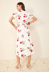 Bijela cvjetna haljina s kratkim rukavima, s motivom ružičastih ruža i zelenog lišća. Detalj elastičnog struka i lepršav, do gležnjeva dugačak kroj.