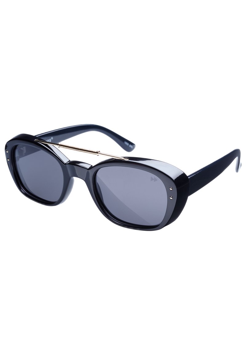 Svarta solglasögon med överdimensionerade, vinklade bågar, mörka linser, guldaccent över näsryggen och en blank yta på plastmaterialet.