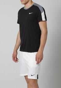 Nike sort trænings-T-shirt med grå og hvide skulderdetaljer, sammen med hvide shorts med sort Nike-logo. Glat, letvægtsstof.