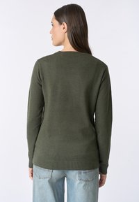 Maglione verde oliva con maniche lunghe, scollatura rotonda e orlo a coste. Indossato con jeans in denim azzurro chiaro, caratterizzati da una vestibilità comoda.