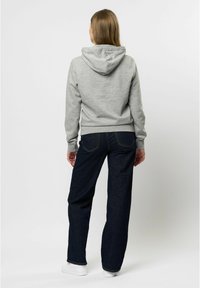 Grå huvtröja med kängurufickor, ribbade manschetter och nederkant, tillsammans med mörkblå vida jeans och vita sneakers.