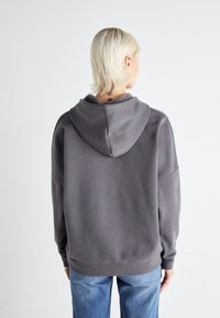 Grå hettegenser med en avslappet passform, myk stoff, ribbede mansjetter og hem; vist fra baksiden, sammen med lyseblå jeans.