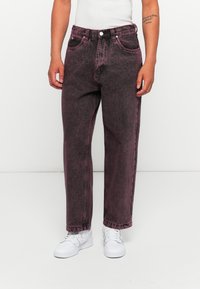 High-waisted, relaxed-fit jeans in a faded burgundy color with a textured finish, featuring front pockets and metal hardware details.