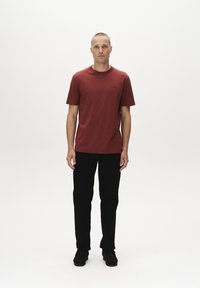 Rød T-shirt med korte ærmer og rund hals, kombineret med sorte slim-fit bukser og sorte sko. Enkel design uden bemærkelsesværdige mønstre eller detaljer.