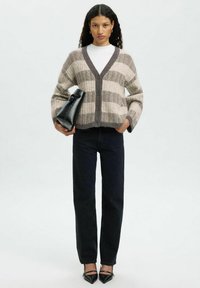 Triibuline kardigan beeži ja halli villaseguga, millel on V-kaelus, nööpidest ees ja üleuuritud varrukad, koos tumedate teksade ja musta kotiga.