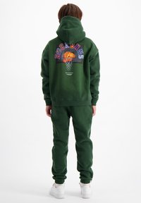 Groene hoodie en joggingbroek set. De hoodie heeft aan de achterkant een kleurrafische basketbalafbeelding. Het materiaal lijkt zacht en heeft een ontspannen pasvorm.