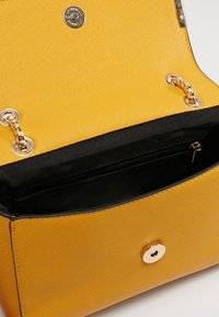 Žlutá kabelka s texturovaným povrchem, zlatým kováním a černou podšívkou. Má kapsu na zip a magnetické zapínání.