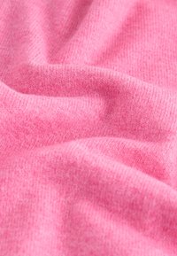 Rosa gestrickter Stoff mit weicher Textur, der ein dezentes Rippenmuster und sanfte Drapierungen aufweist und eine glatte und gleichmäßige Oberfläche zeigt.