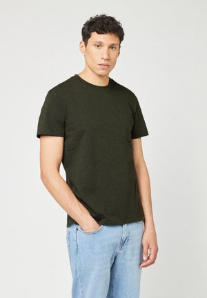 Dark green crew-neck t-shirt in a soft, textured fabric with short sleeves and a chest pocket. Worn with light blue jeans.