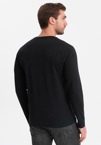 Schwarzes Langarm-T-Shirt aus weichem Stoff mit Rundhalsausschnitt, schlanker Schnitt und minimalistisches Design.