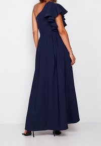 Marinblå golvlång klänning, asymmetrisk design med volangdetalj, figursydd bodice och plisserad kjol, tillverkad av mjukt tyg.