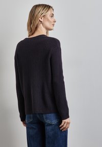 Dunkellila gestrickter Pullover mit strukturiertem Rippmuster, langärmlig und mit lässiger Passform, kombiniert mit blauen weit geschnittenen Jeans.