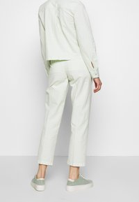 Light green, textured outfit featuring a cropped button-up shirt and straight-leg pants. Accented with subtle stripes. Paired with green sneakers.