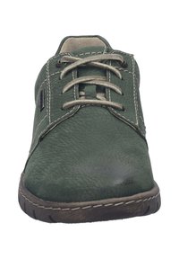 Zielone skórzane buty za sznurówki z teksturowaną powierzchnią, kontrastowym beżowym przeszyciem i gumową podeszwą z poziomymi rowkami.