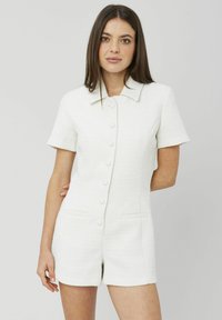 Combinaison courte blanche texturée avec un col, des manches courtes et une fermeture à six boutons à l'avant, comportant deux poches avant.