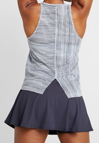 Vue de dos d'une personne portant un haut sans manches rayé noir et blanc avec un ourlet fendu et une jupe évasée foncée.