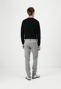 Suéter negro de canalé, pantalones a rayas grises con dos bolsillos traseros y tenis blancos con acentos negros, vistos desde atrás sobre un fondo sencillo.