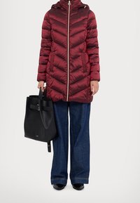 Burgundy puffer coat with chevron design, zip closure, and hood; paired with wide-leg denim pants and a black leather bucket bag.